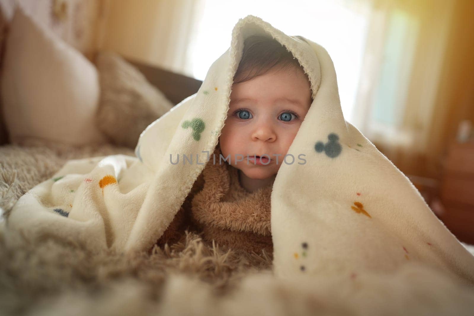 Cute baby girl crawling on bed under the blanket. Adorable kid portrait. 6 month old child. Childhood concept. High quality photo