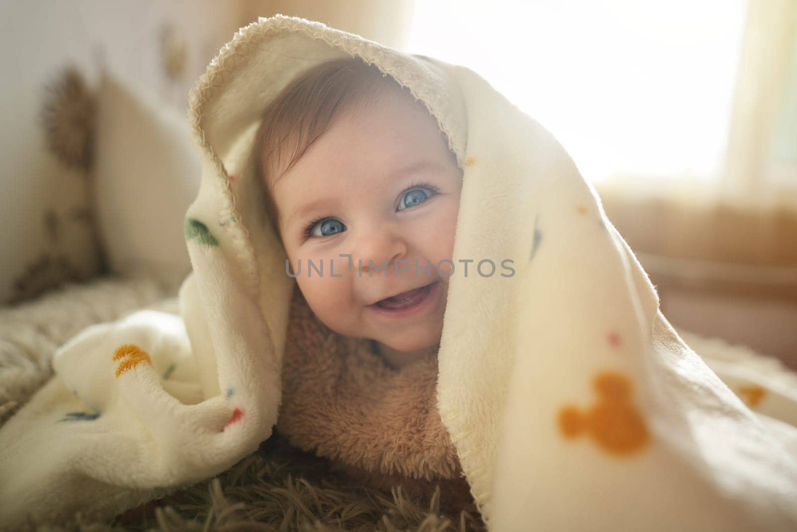 Smiling baby girl crawling on bed under the blanket. Adorable kid portrait. 6 month old child. Childhood concept. High quality photo