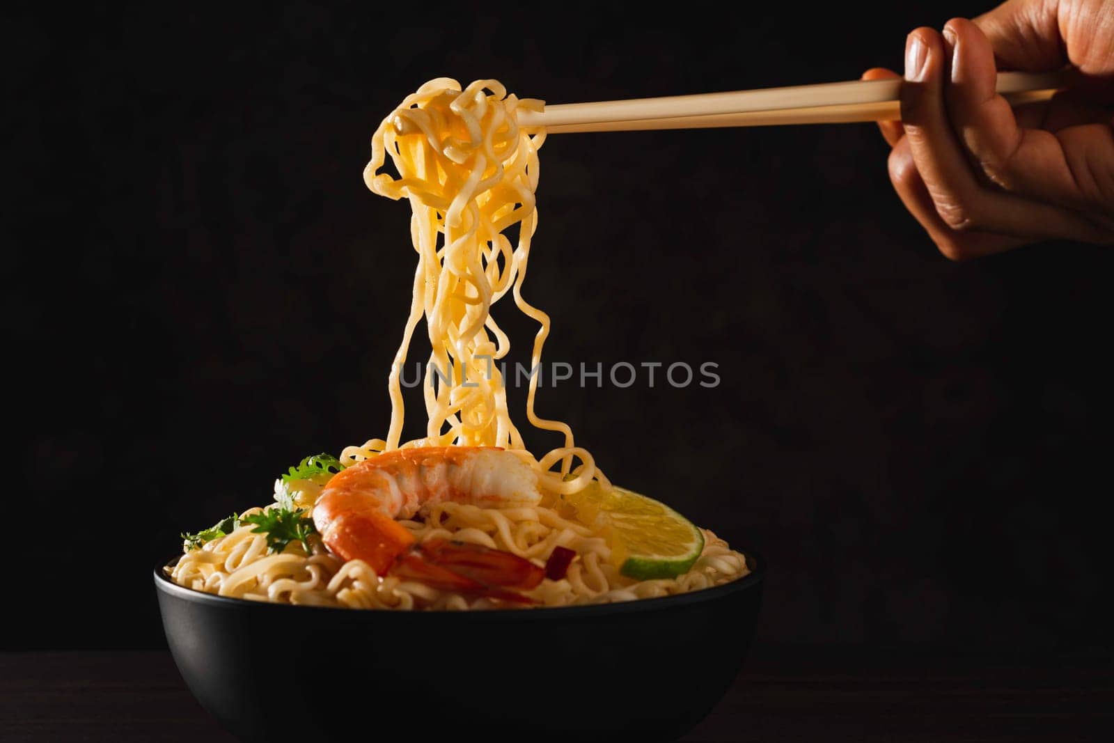 Hand using chopsticks pickup instant noodles with smokes isolated on black background.