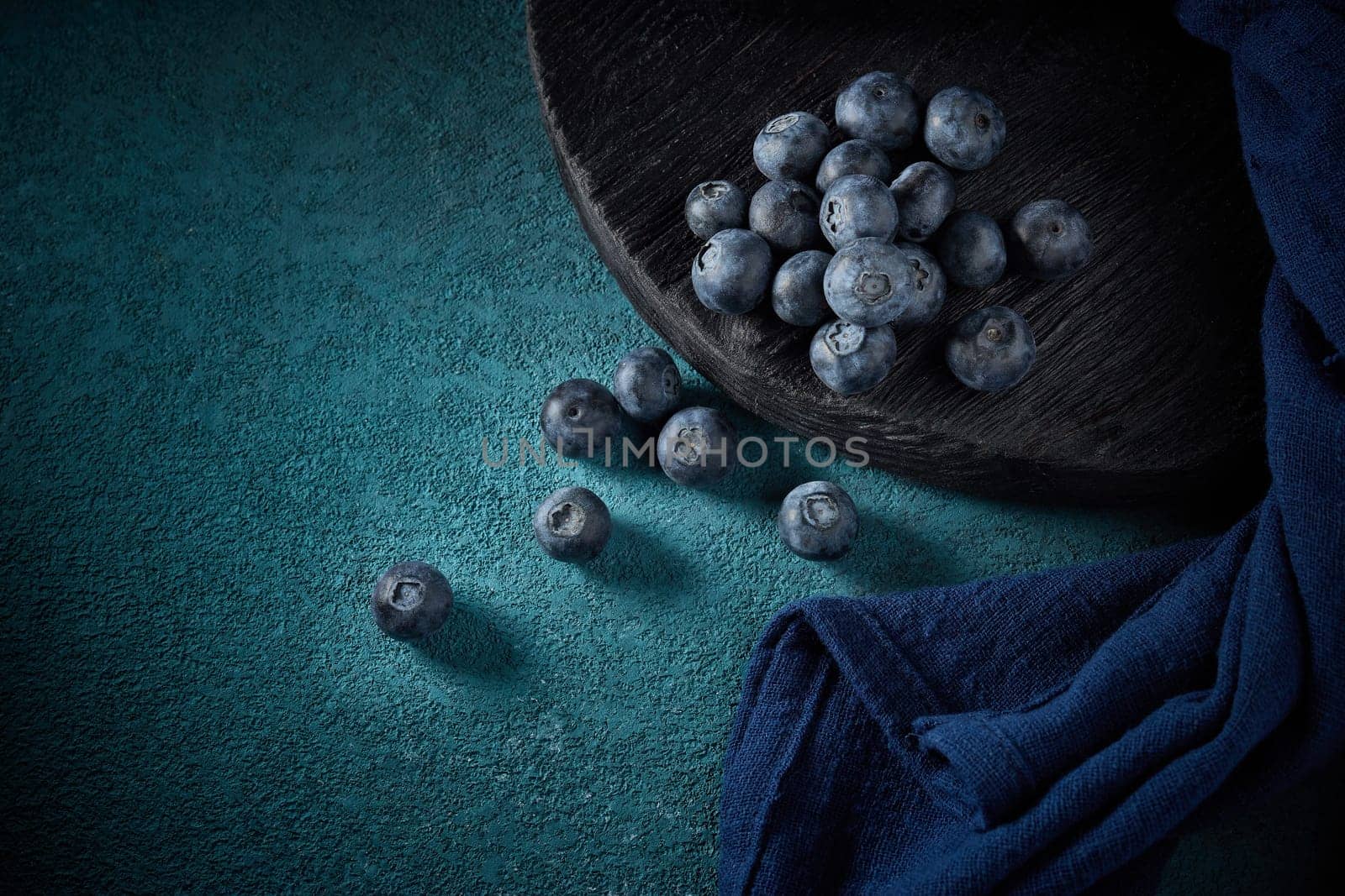 Ripe blueberries (bog whortleberry, great bilberry) on black wooden board on dark blue background. Top view