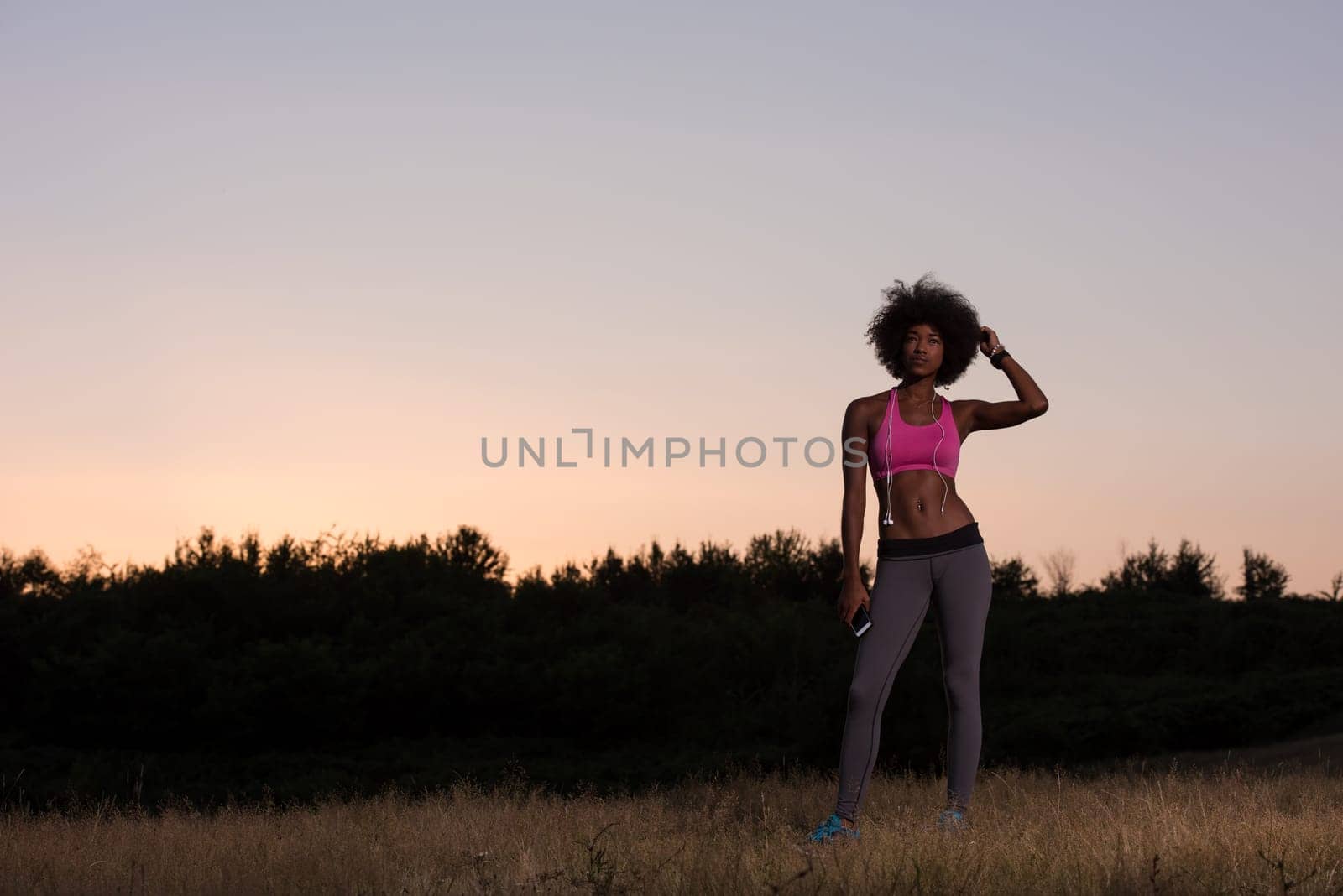 portrait of a young beautiful african american woman with headphones and mobile phone jogging in nature beautiful summer night