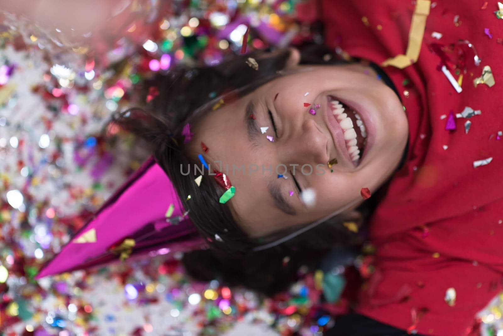 Happy kid celebrating party with blowing confetti while lying on the floor