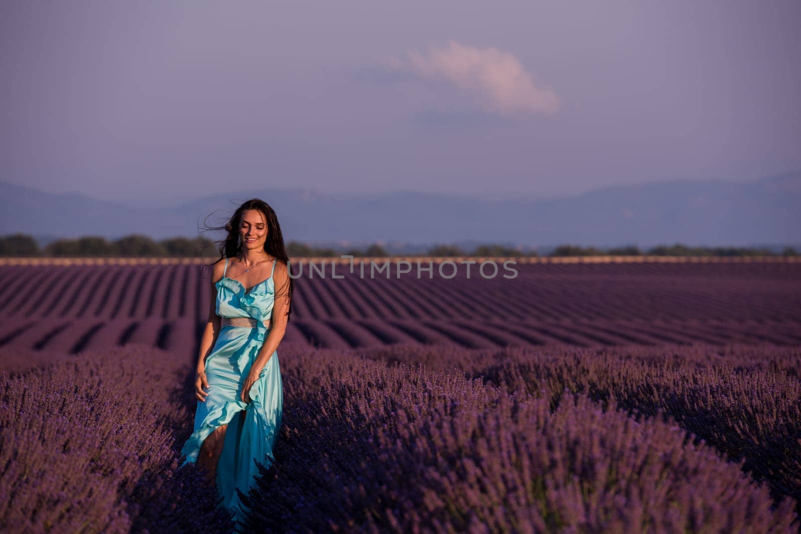 portrait of a beautiful young woman in cyand dress relaxing and having fun on wind at purple lavander flower field