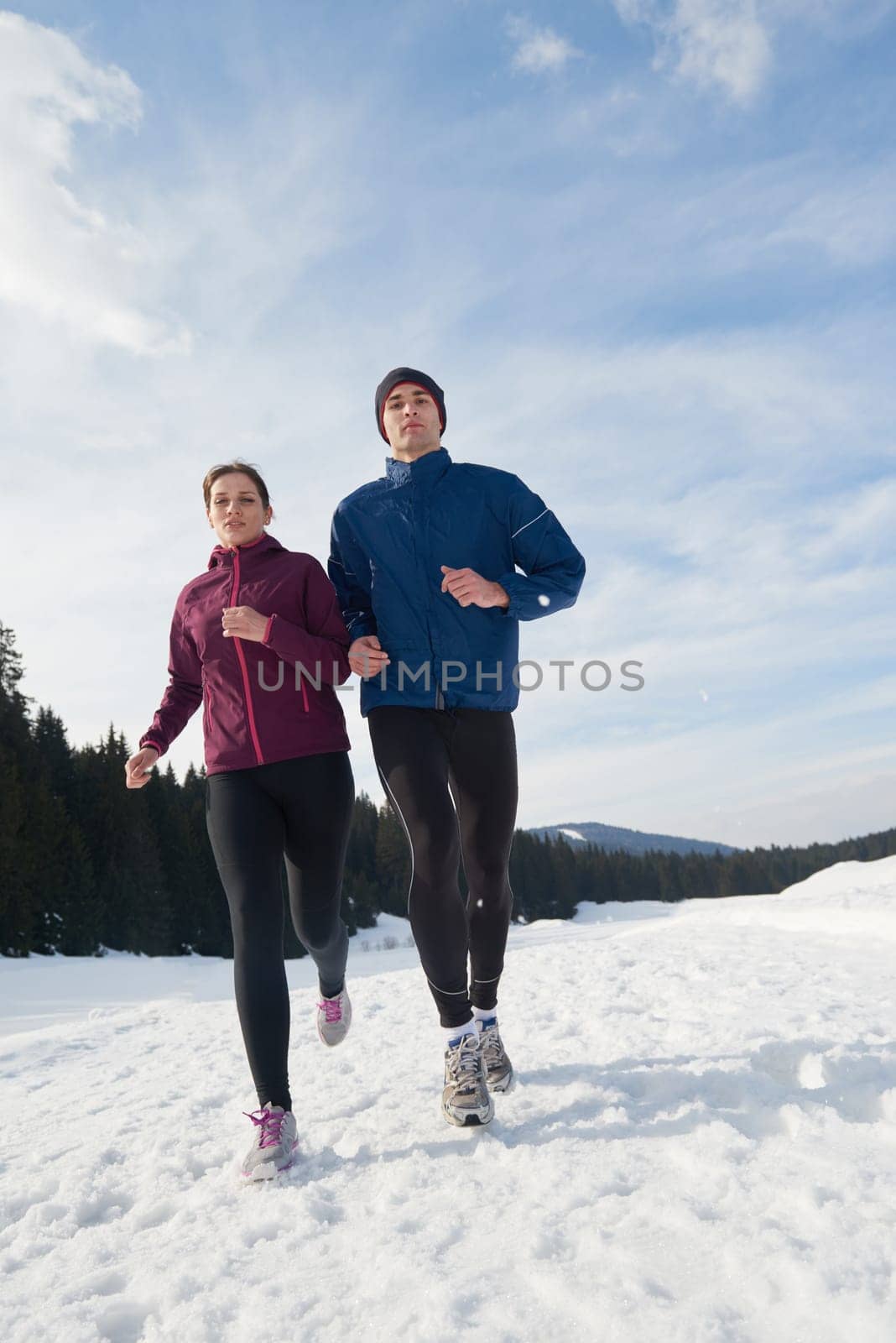 healthy young couple jogging outside on snow in forest. athlete running on  beautiful sunny winter day