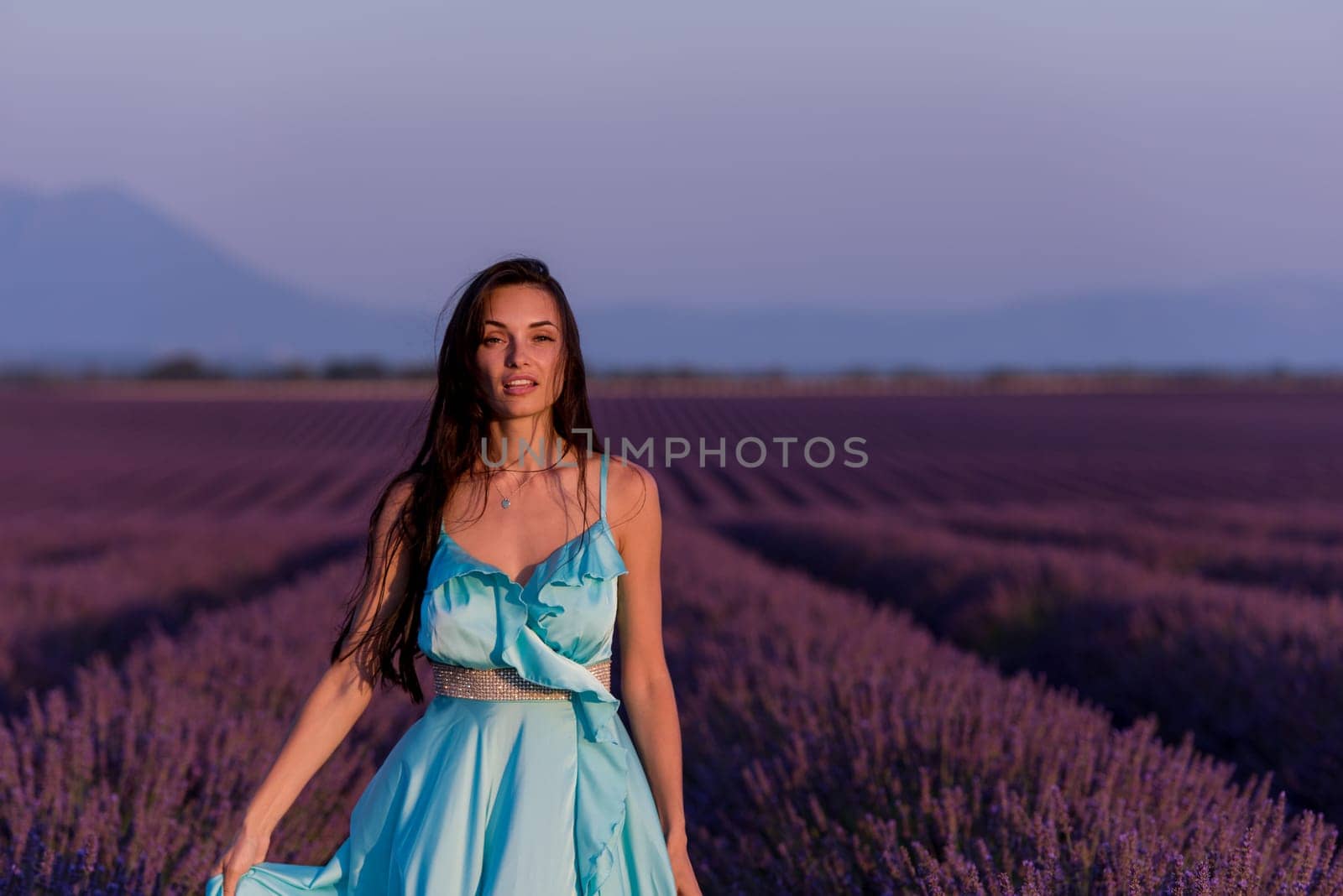 portrait of a beautiful young woman in cyand dress relaxing and having fun on wind at purple lavander flower field