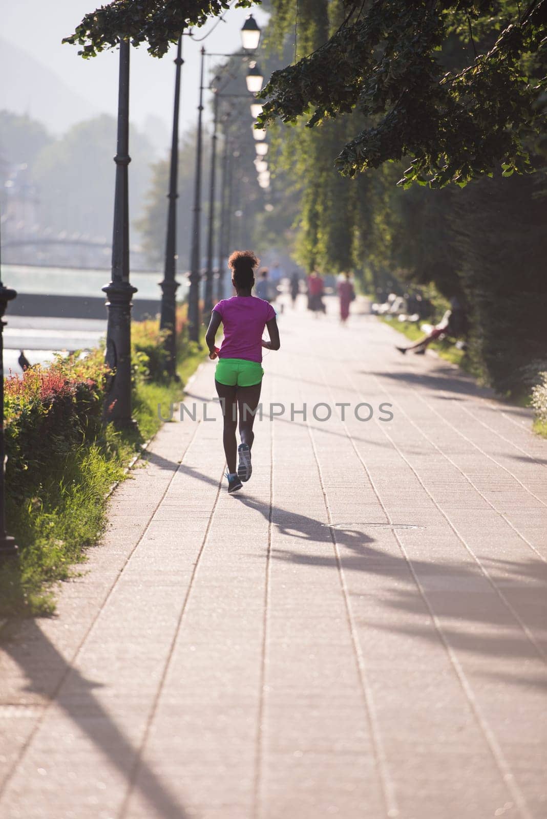 Beautiful young sporty african american woman running at early morning jogging with city sunrise scene in background