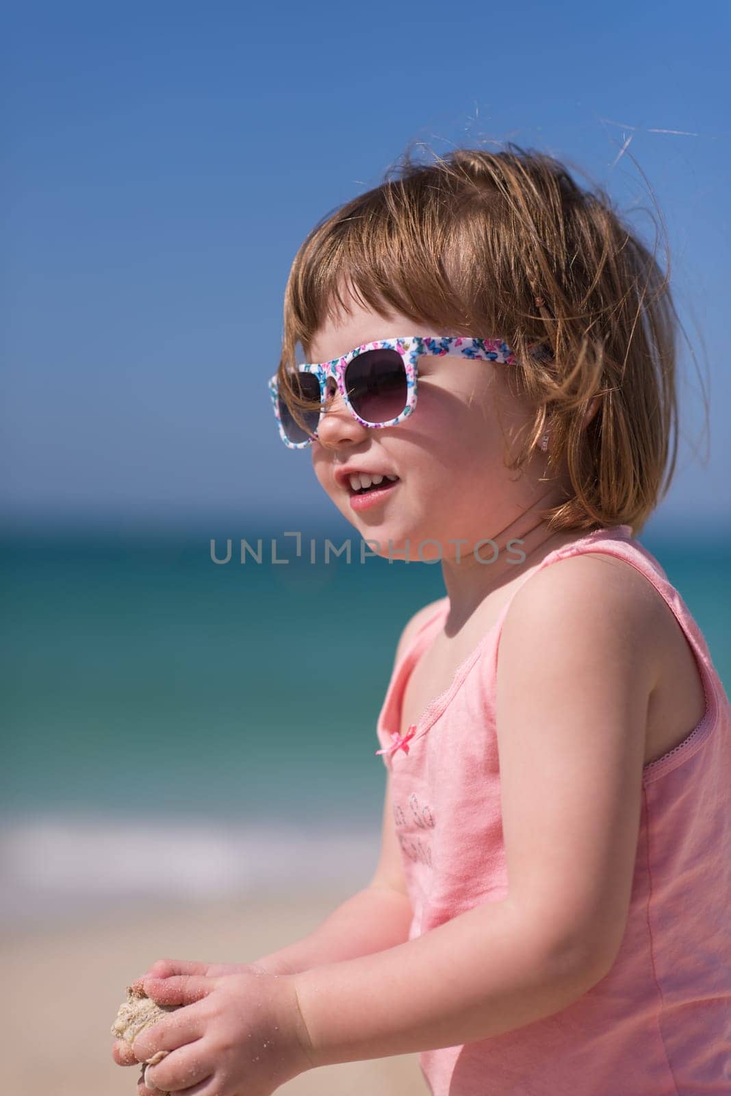 happy little girl at the seaside in the summer.Adorable little girl at beach during summer vacation. Happy baby with sunglasses by the sea or ocean