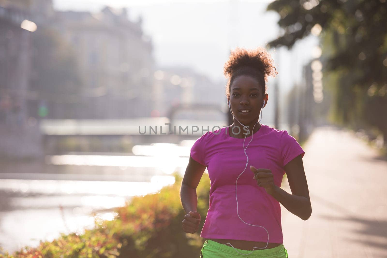 Beautiful young sporty african american woman running at early morning jogging with city sunrise scene in background