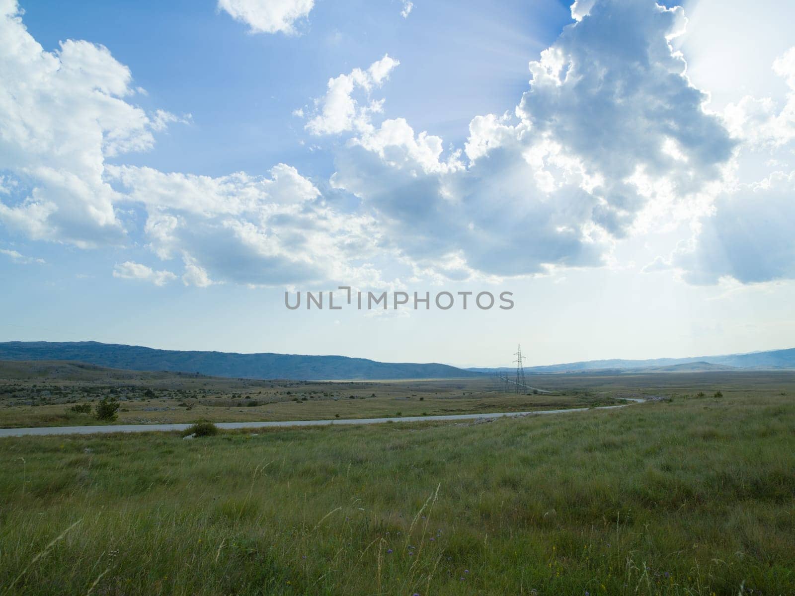 Evening summer landscape with green grass, road and clouds