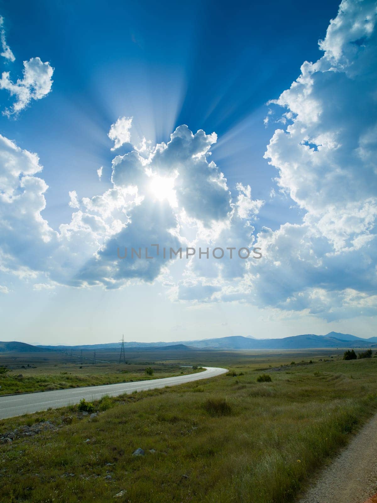 Evening summer landscape with green grass, road and clouds
