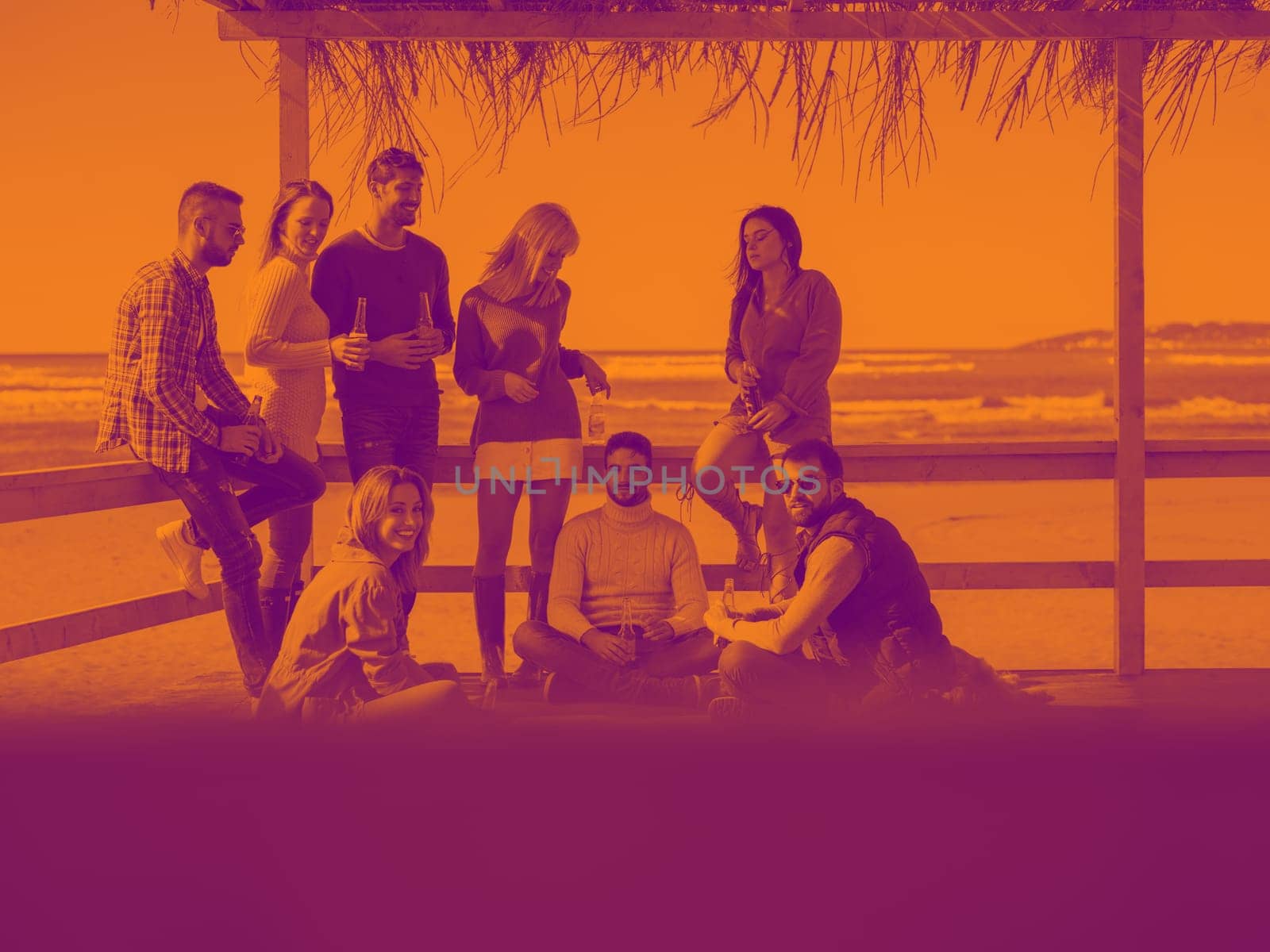 Happy Group Of Friends Hanging Out At Beach House having fun and drinking beer on autumn day