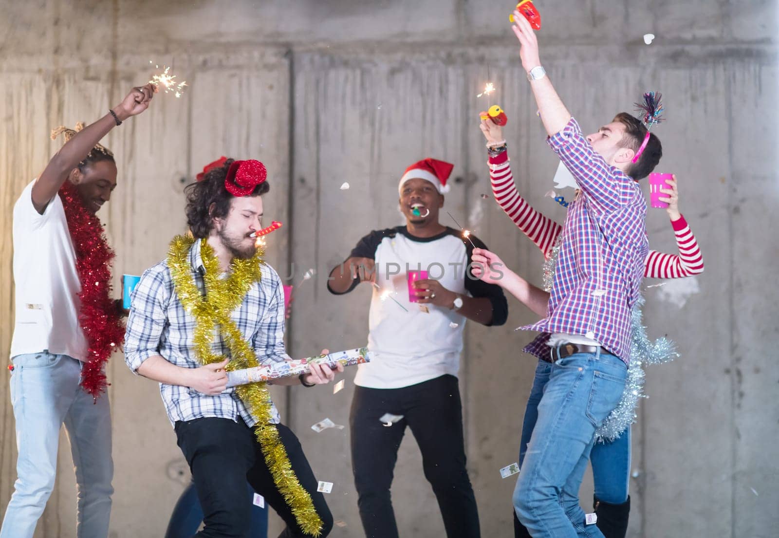 multiethnic group of young happy casual business people dancing and having confetti party while celebrating new year eve in front of concrete wall at new startup office