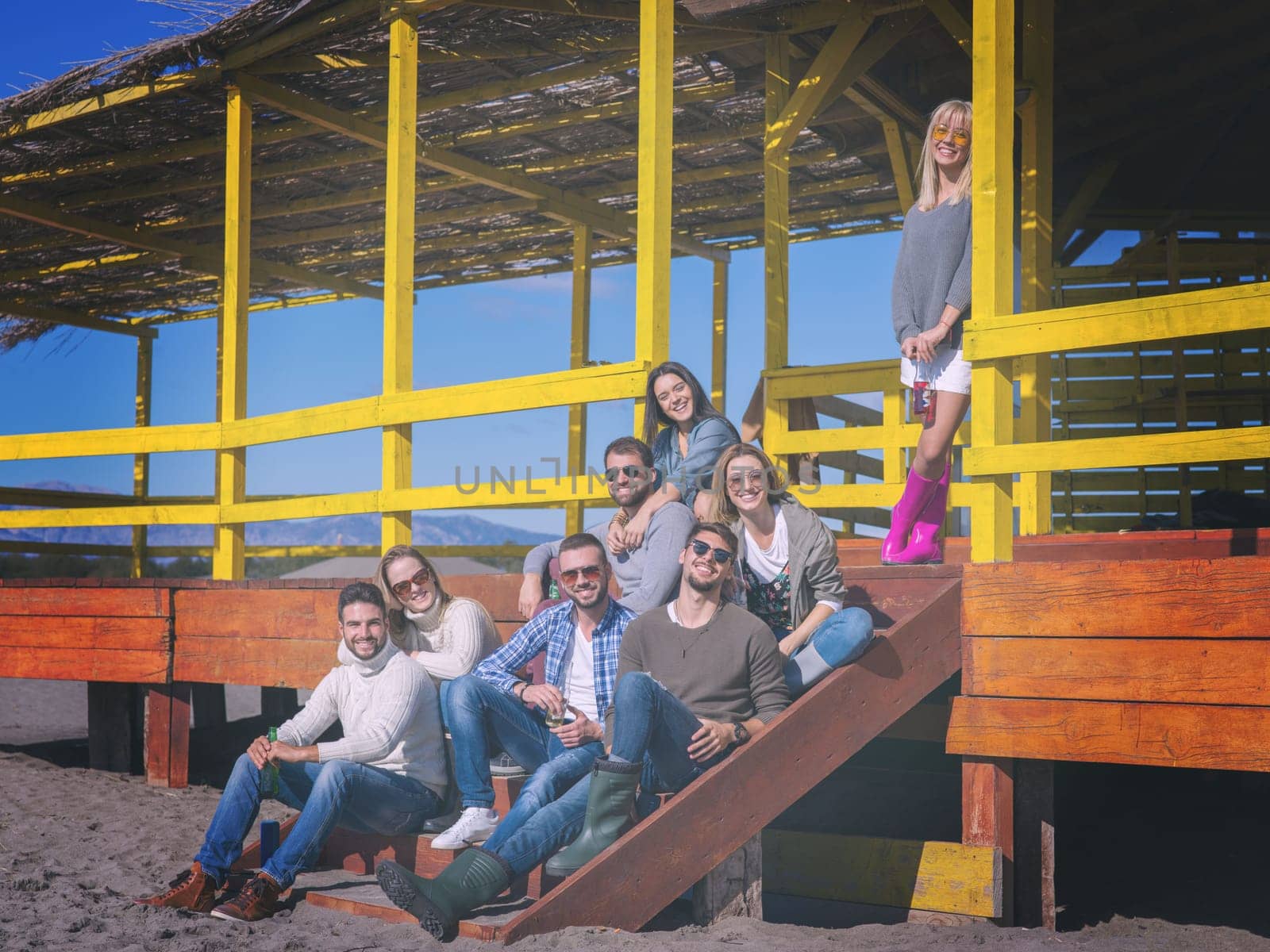 Happy Group Of Friends Hanging Out At Beach House having fun and drinking beer on autumn day colored filter