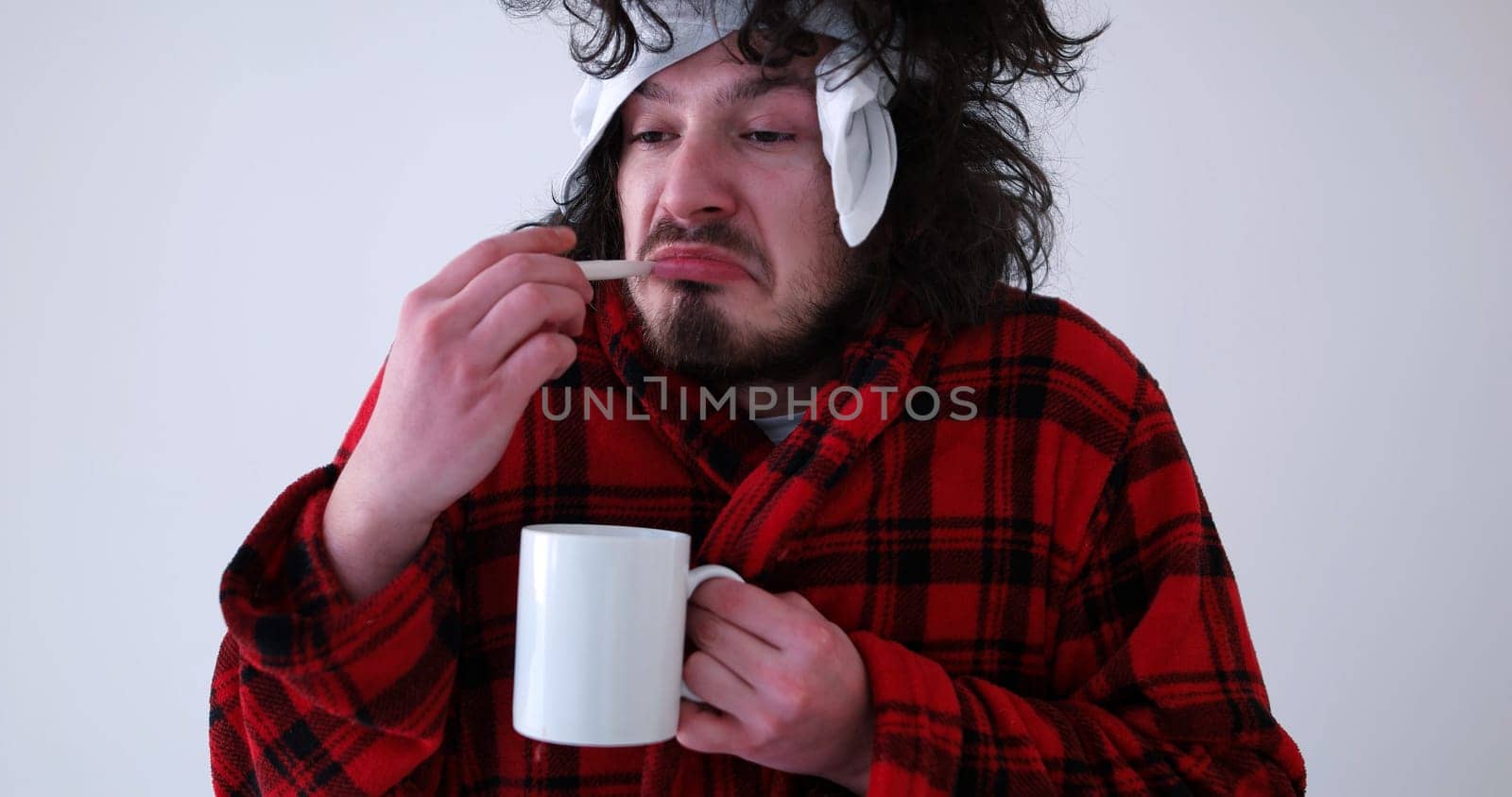 young Man with flu and fever wrapped holding cup of healing tea isolated over white