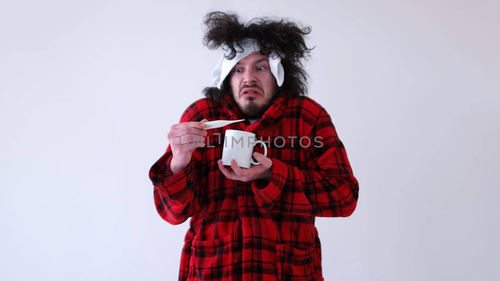 young Man with flu and fever wrapped holding cup of healing tea isolated over white