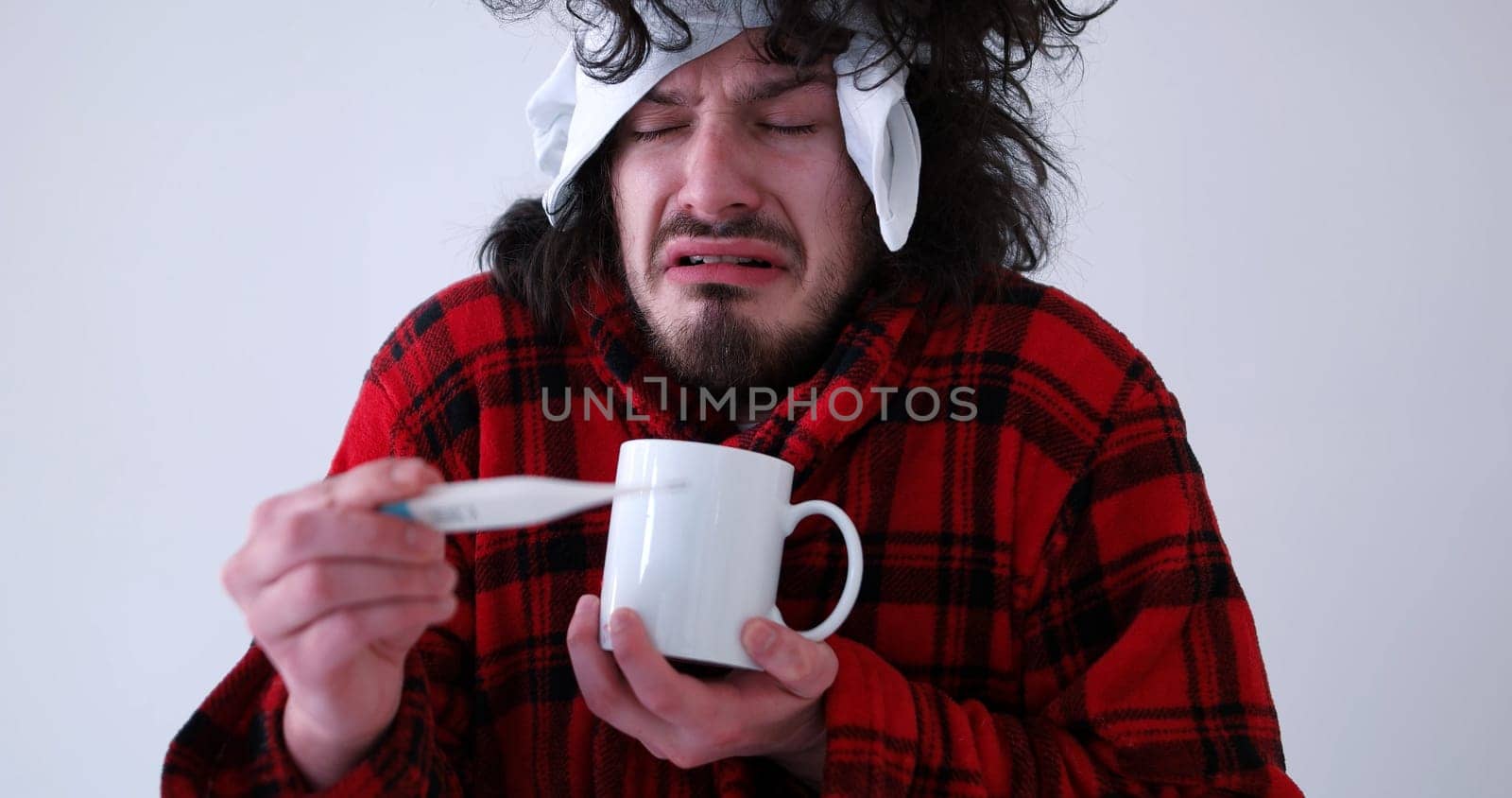 young Man with flu and fever wrapped holding cup of healing tea isolated over white