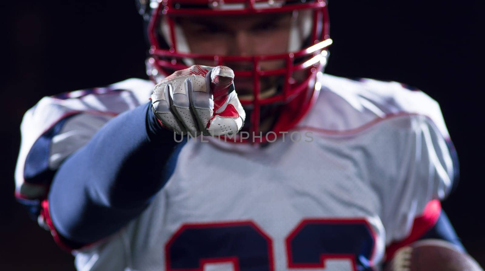 portrait of confident American football player holding ball while standing on field at night
