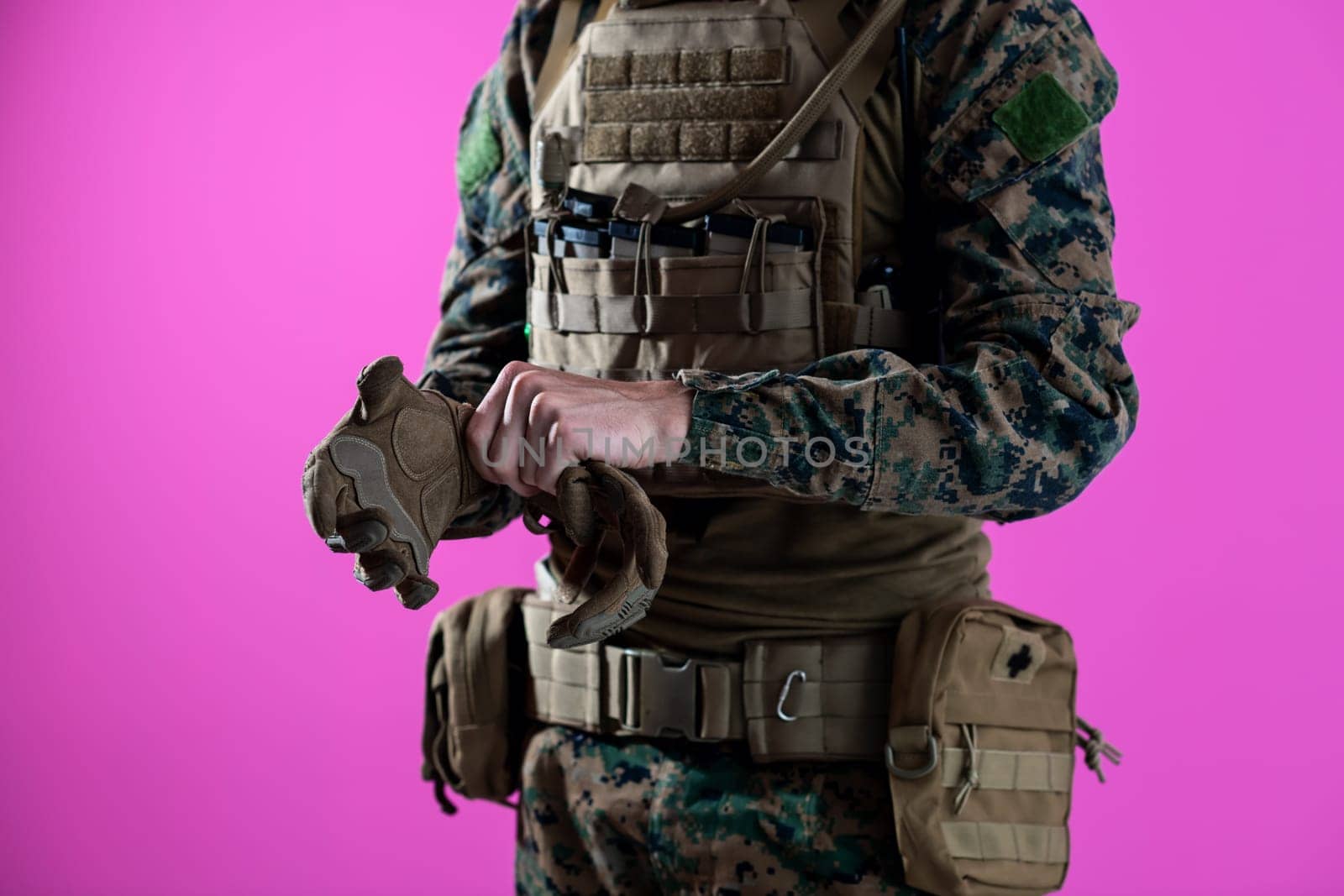 closeup of modern warfare soldier hands putting protective battle gloves pink background