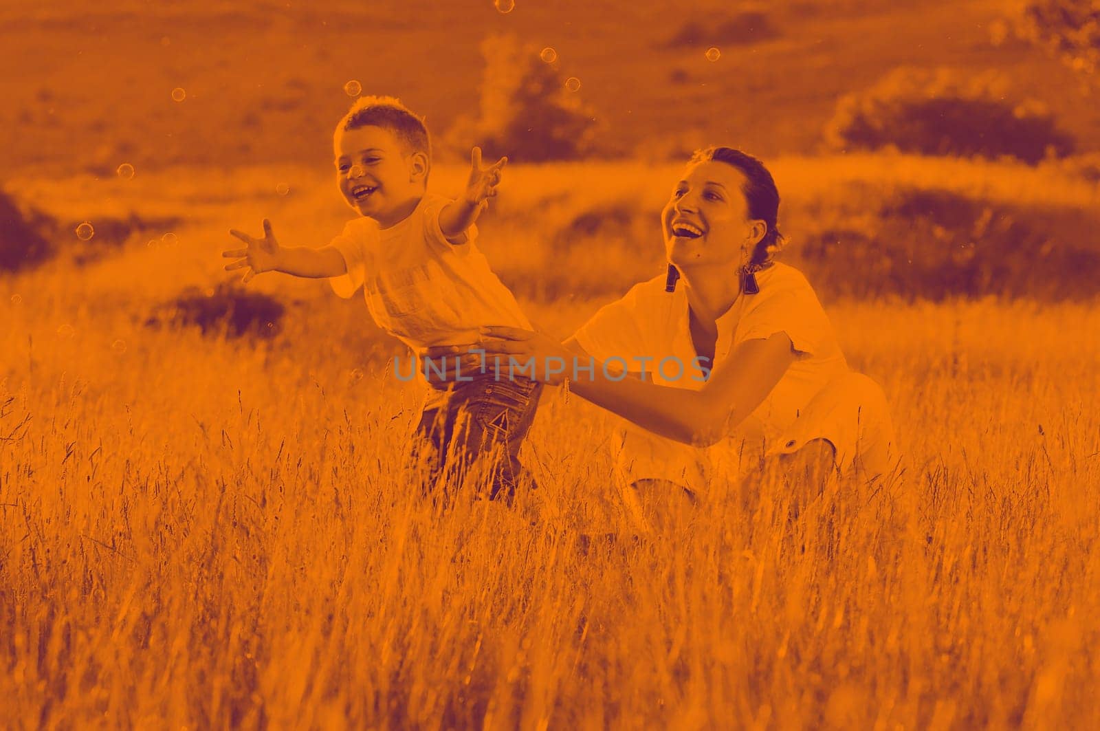 happy child and woman outdoor playing with soap bubble on meadow duo tone