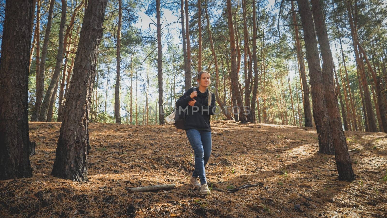 Toned photo of tired female tourist with heavy backpack walking on hiking route in forest.