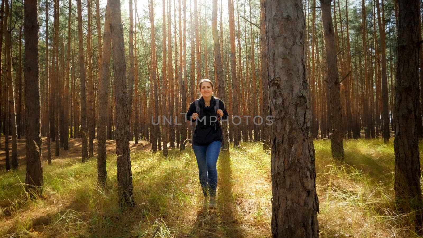 Beautiful smiling woman enjoying hiking in pine forest on sunny autumn day.
