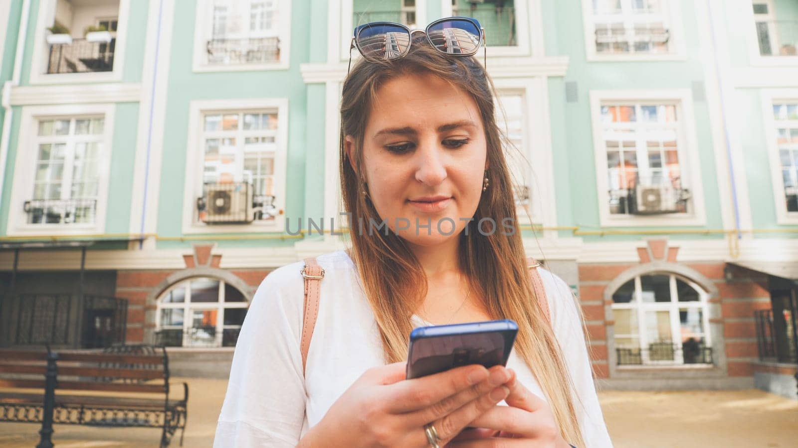 Toned portrait of young girl with smartphone against old building on city street.