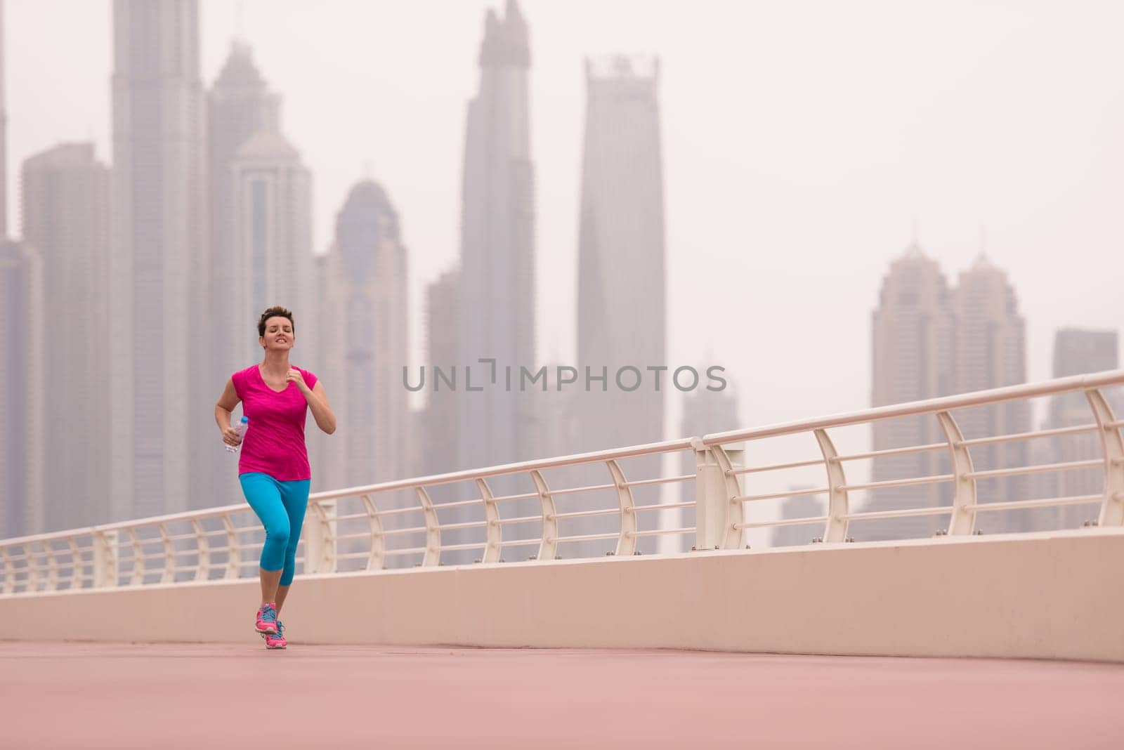 very active young beautiful woman busy running on the promenade along the ocean side with a big modern city in the background to keep up her fitness levels as much as possible