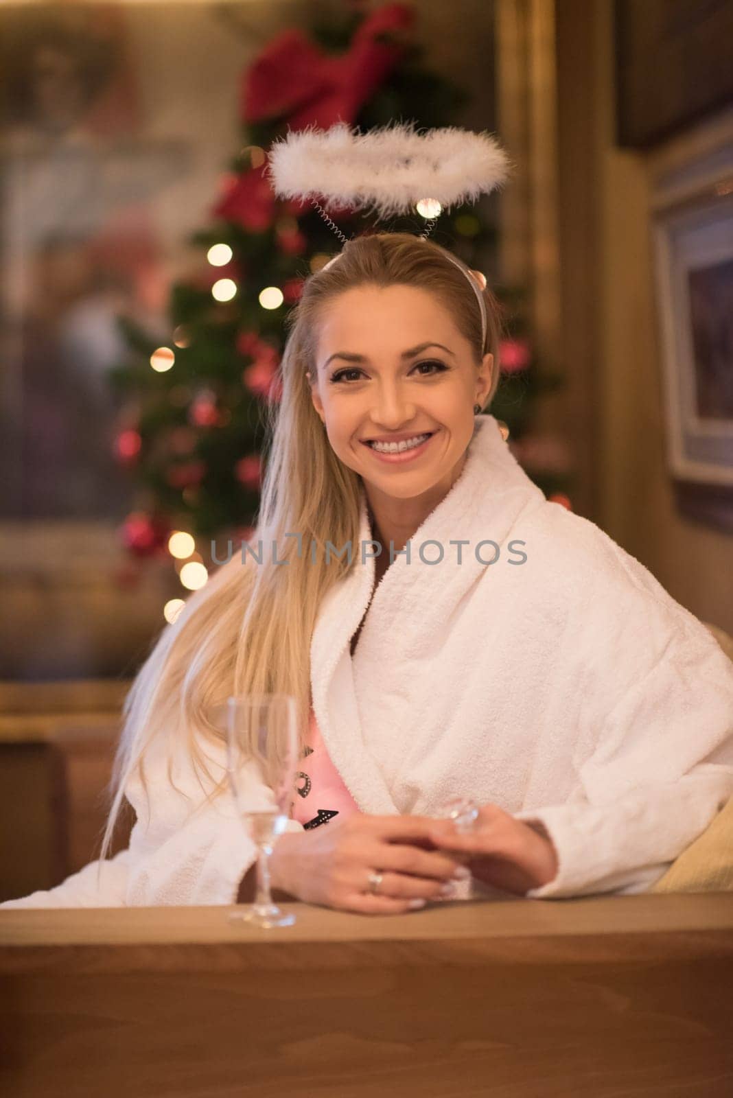 people, and relaxation concept   beautiful young woman in bath robe drinking champagne at spa over holidays lights background