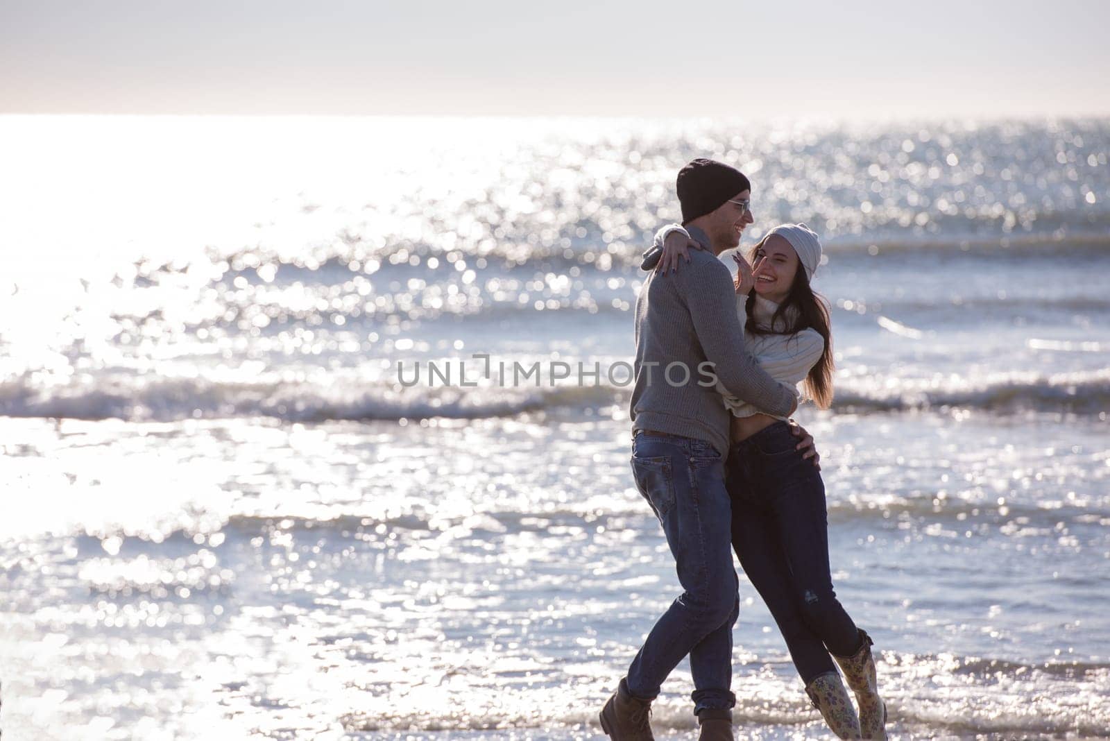 Young couple having fun walking and hugging on beach during autumn sunny day