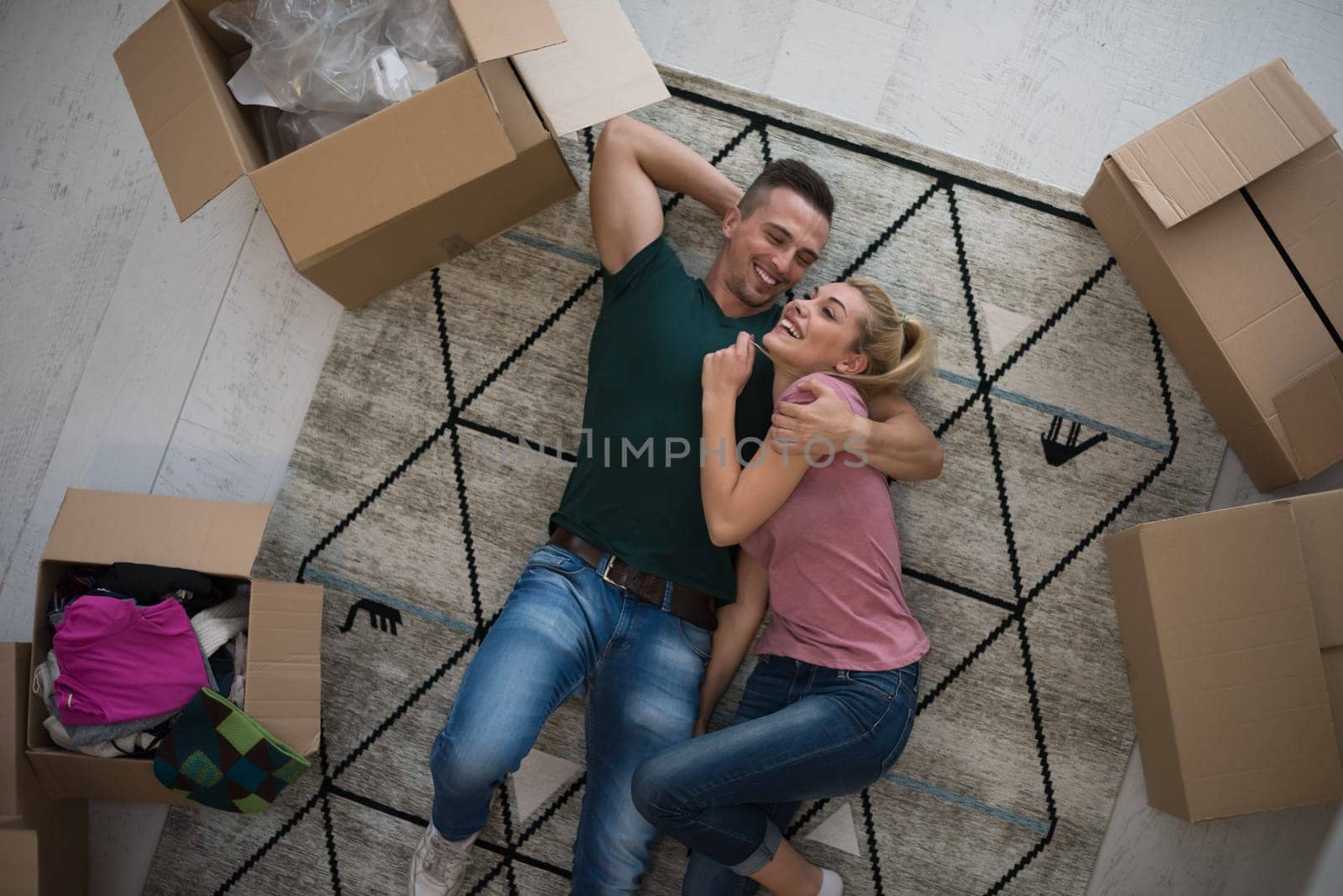Top view of attractive young couple moving, holding hands, looking at camera and smiling while lying among cardboard boxes