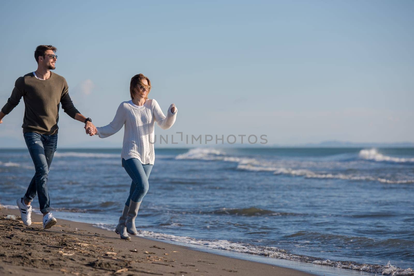 Young couple having fun walking and hugging on beach during autumn sunny day