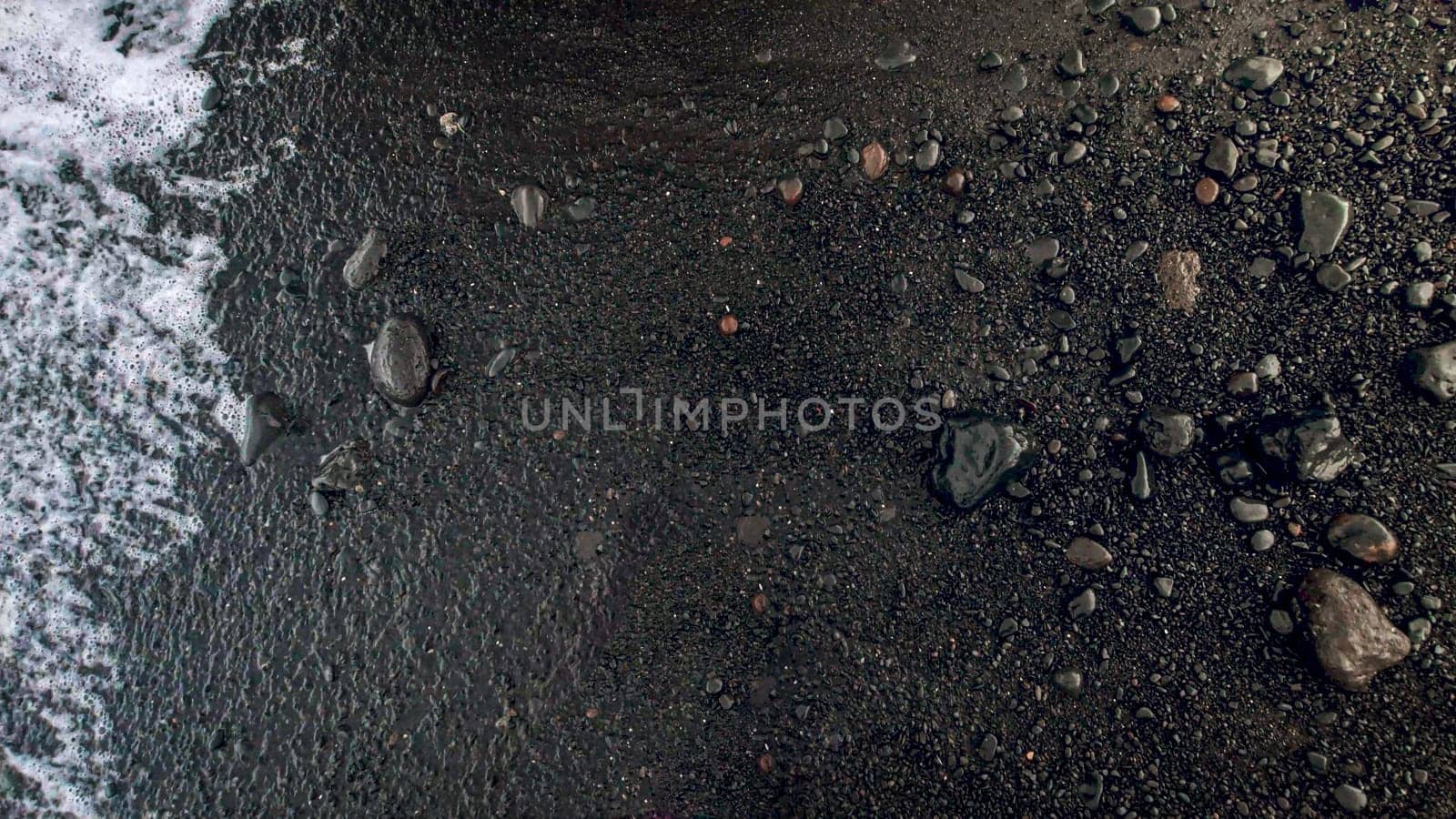Closeup image of wet black volcanic sand and pebbles on ocean beach.