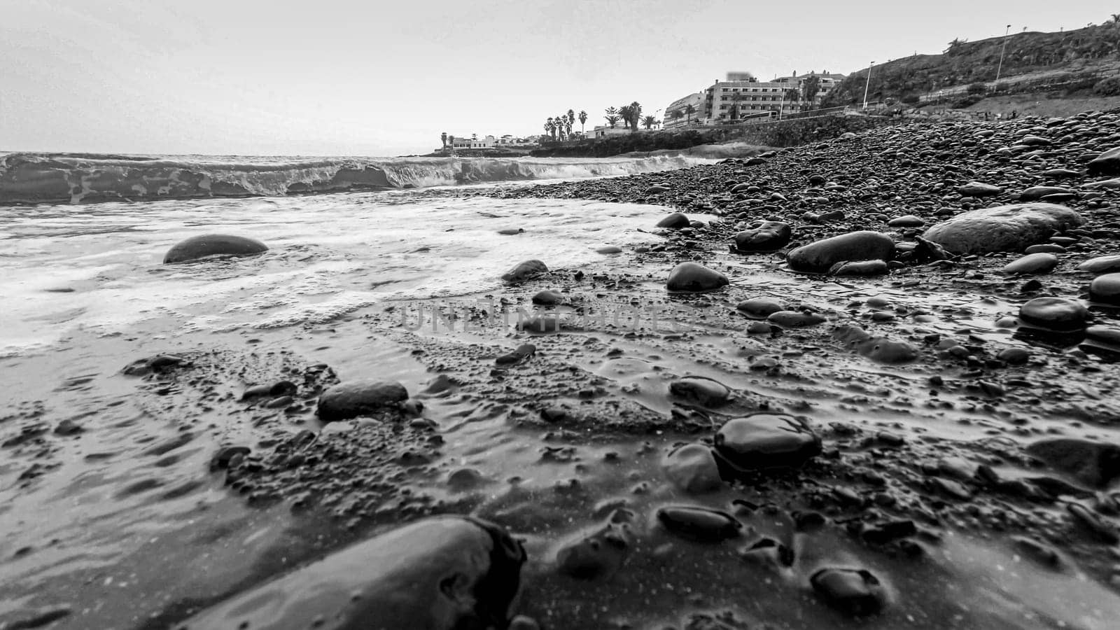 Black adn white seascape of ocean waves rolling small rocks and pebbles on the shore.