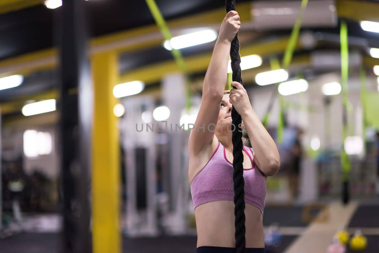 young muscular woman doing rope climbing in cross fitness gym