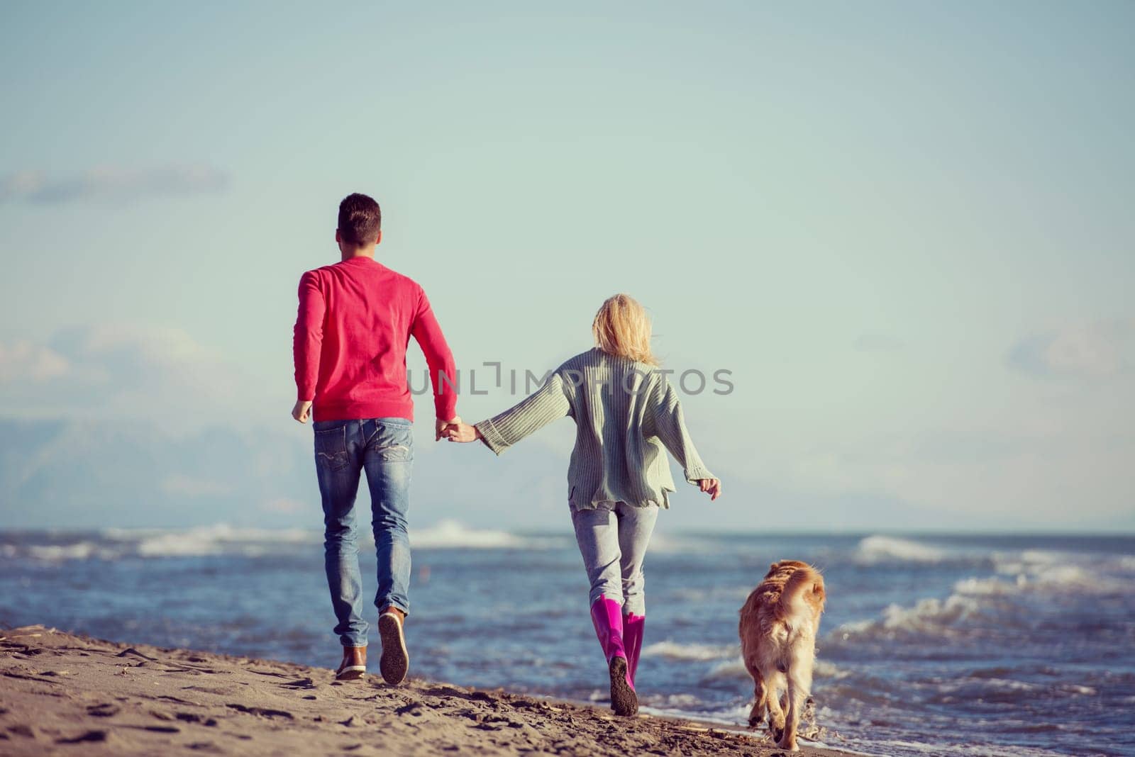 Couple Running On The Beach Holding Their Hands with dog On autmun day