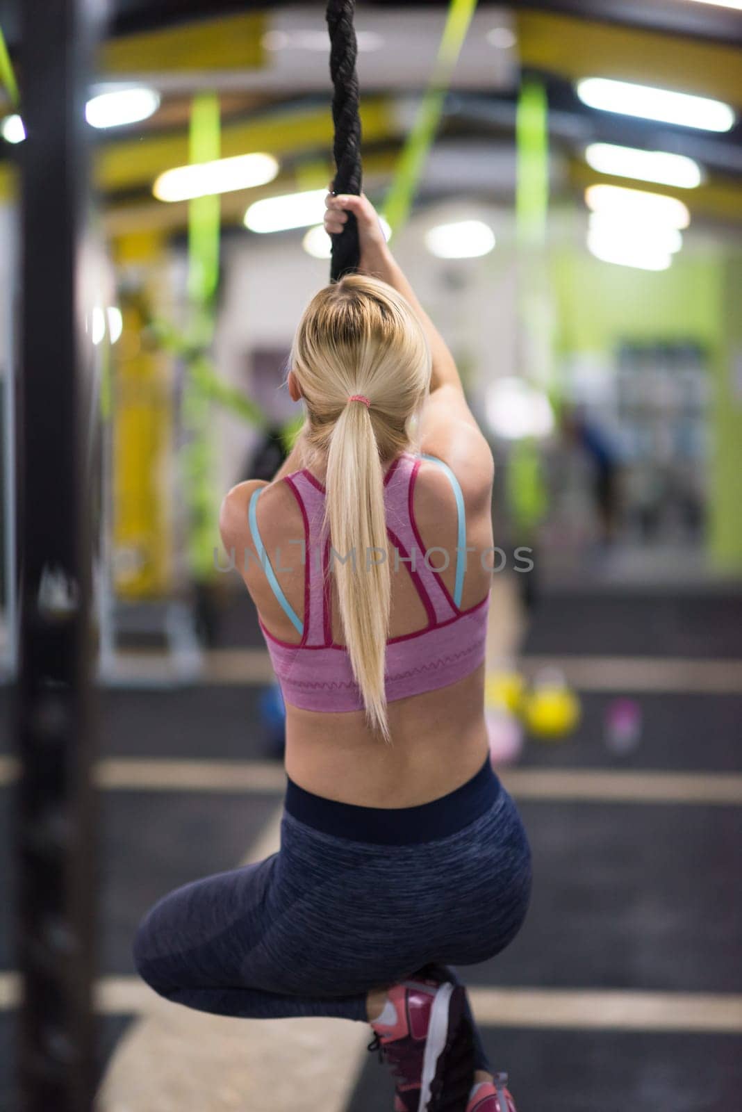 young muscular woman doing rope climbing in cross fitness gym