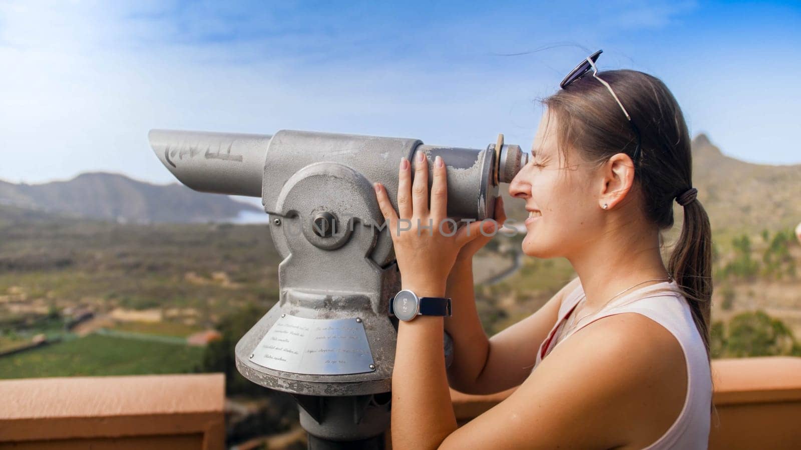 Portrait of happy smiling female tourist looking on ountains through coin operated binoculars.