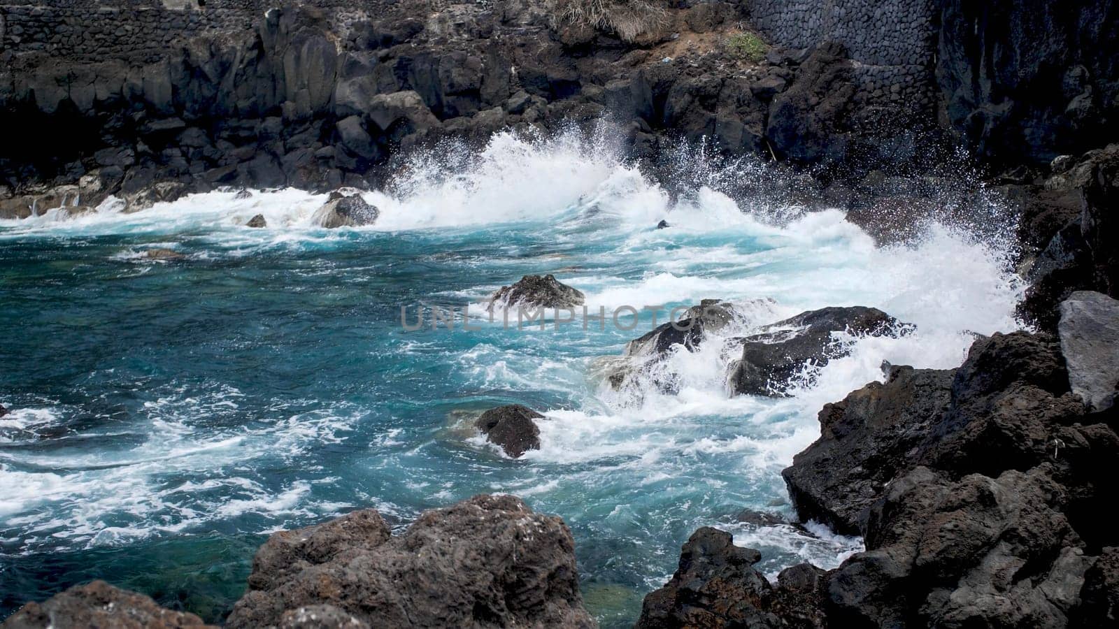 Seascape of powerful turquoise ocean waves breaking on black volcanic cliffs on the coast.