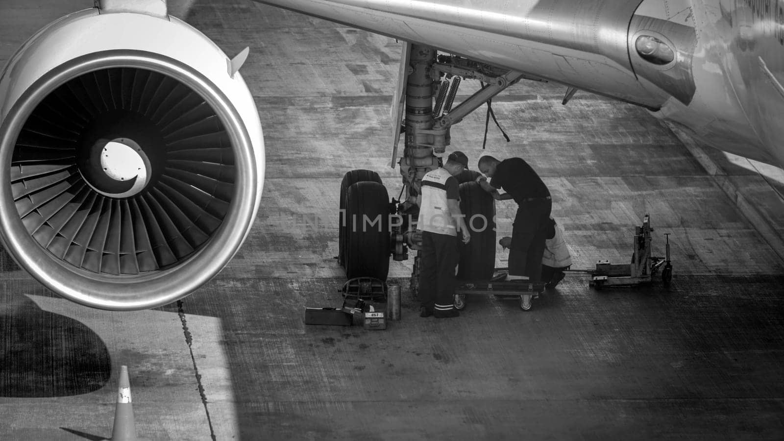 Black and white image of maintenance ground crew checking and repairing airplane chassis wheels before taking off.