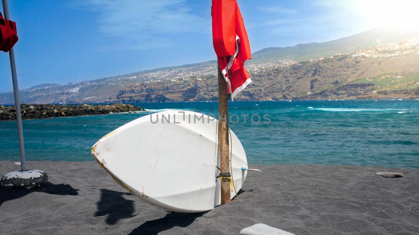 White surfboard and lifeguard post on the ocean beach wth black volcanic sand.