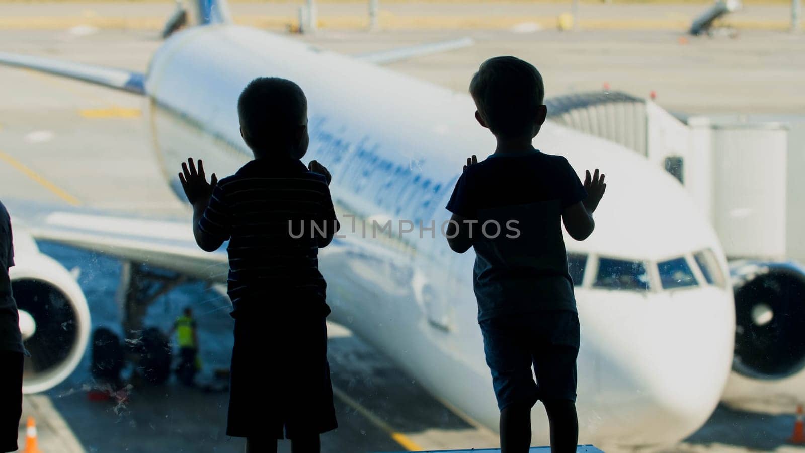 Silhouetes of two little boy looking on airplane through window before flight.
