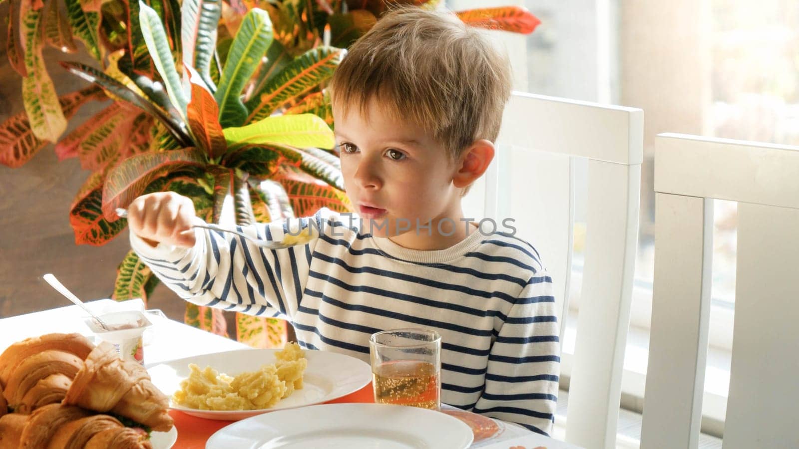 Portrait of little boy eating porridge or mashed potate in dining room.