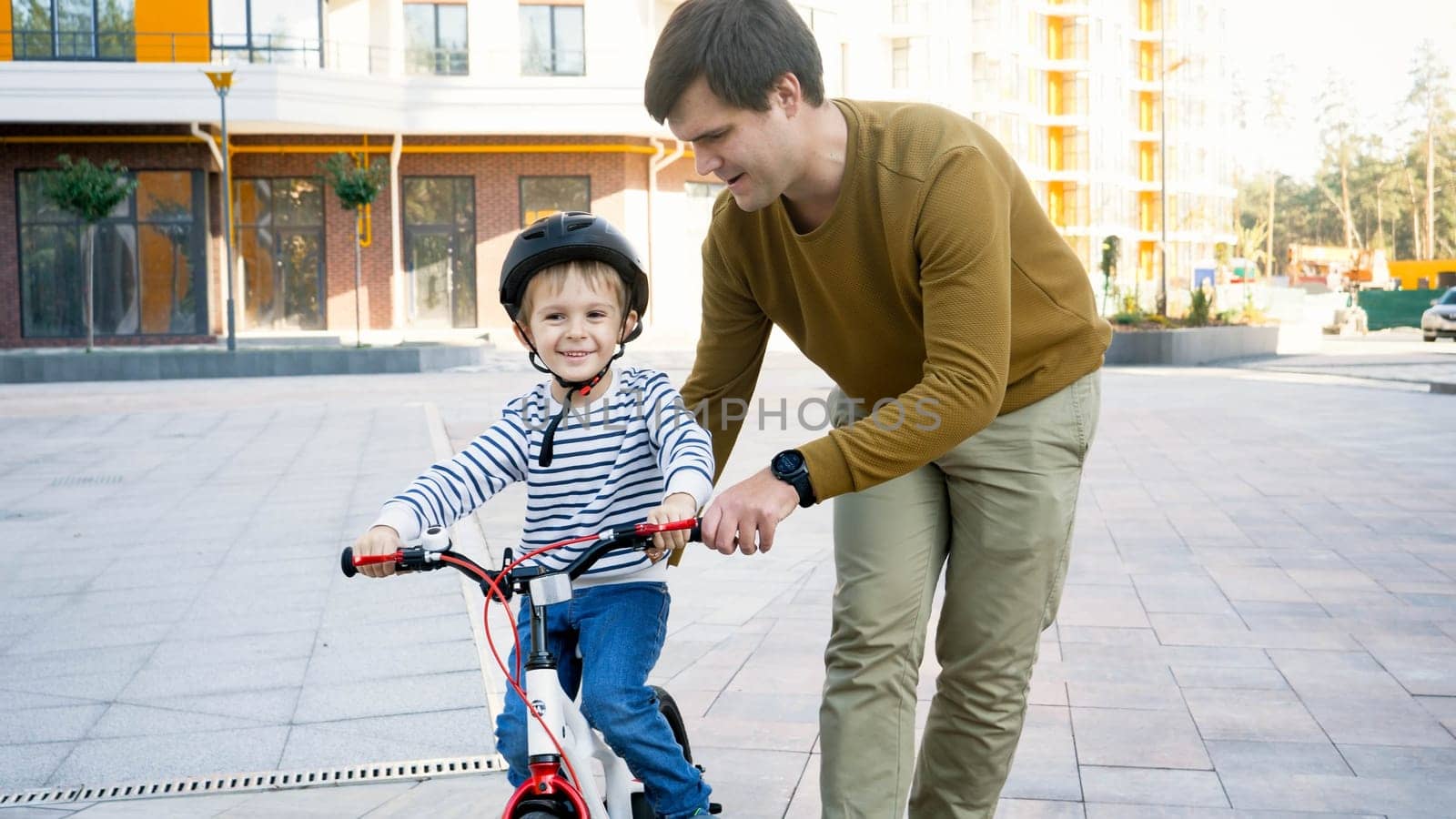 Portrait of smiling little boy learning riding his first bicycle with young father.