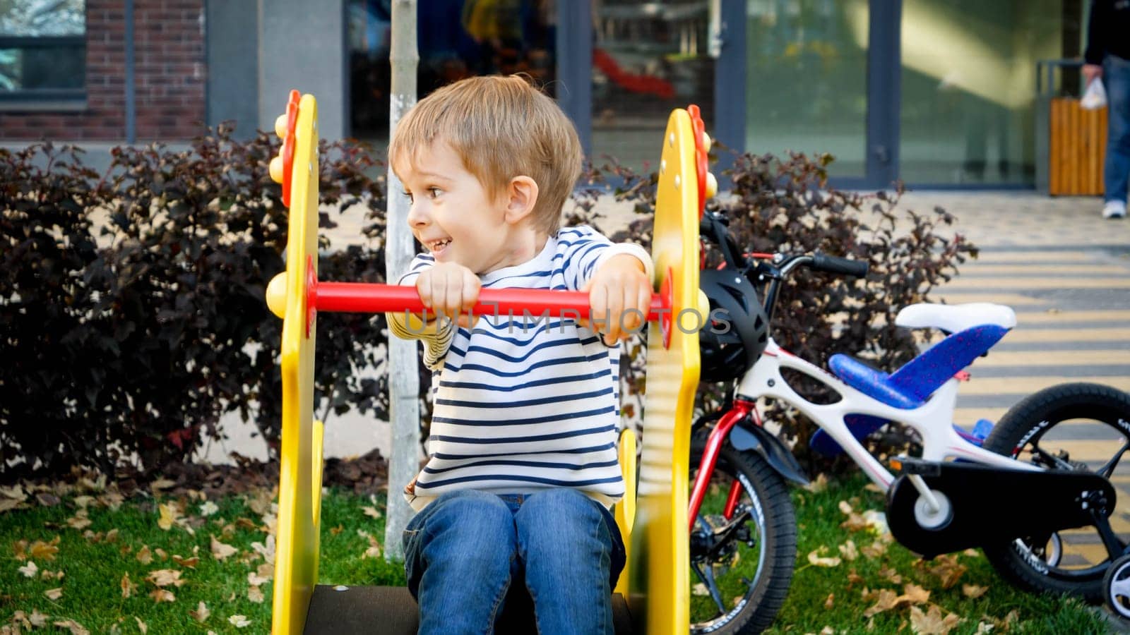 Portrait of happy laughing little boy riding on children playground at park.