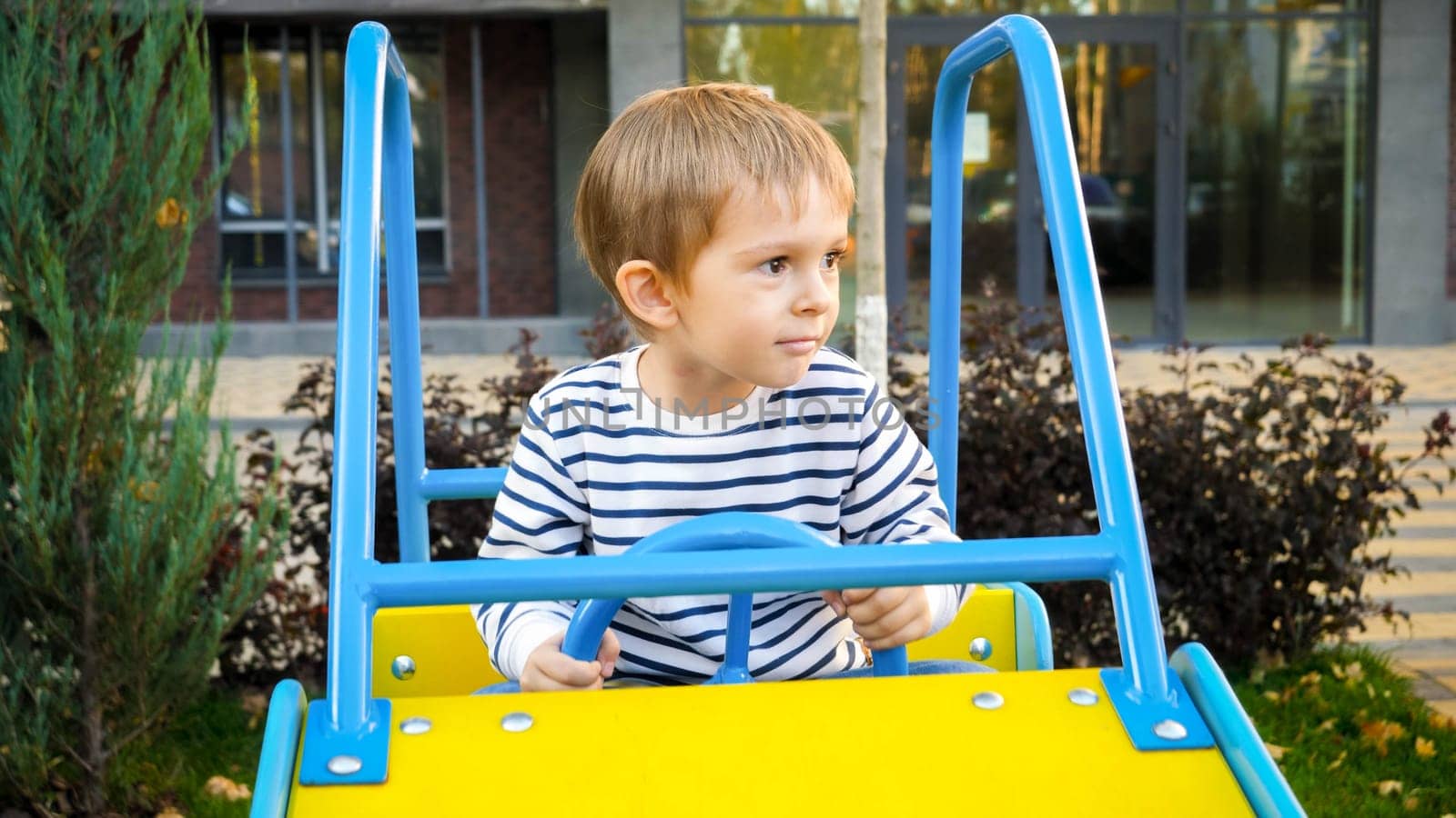 Happy smiling boy riding in big toy car on children playground.