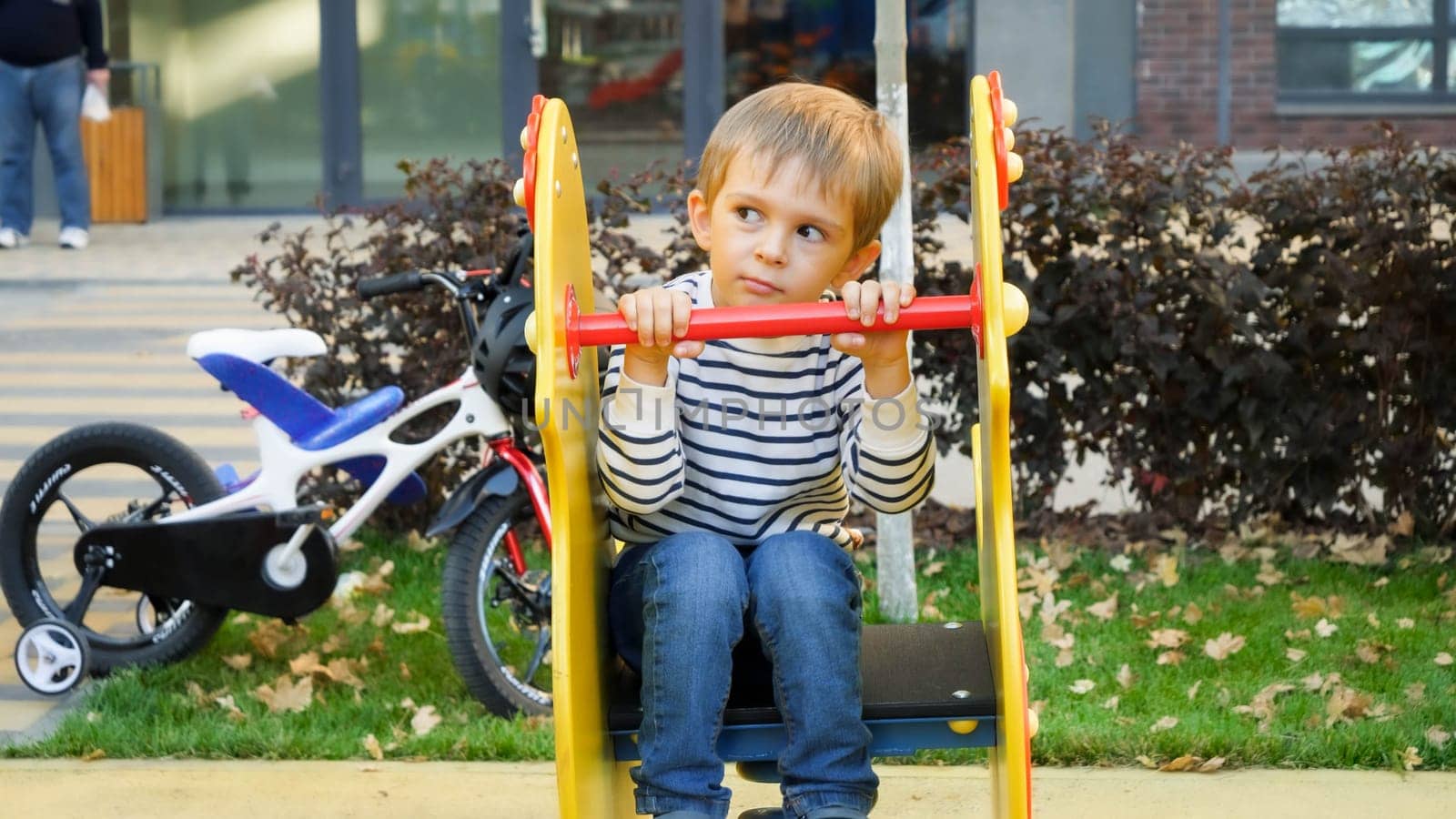 Portrait of thoughtful little boy itting on children playground at park.