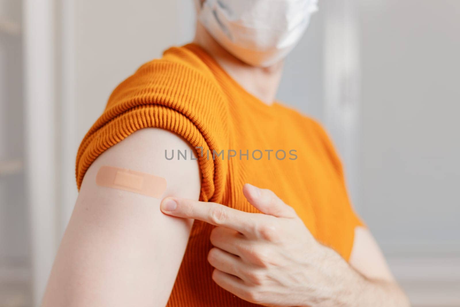 Man in mask showing his shoulder with bandage after getting a vaccination during covid-19 immunization program.