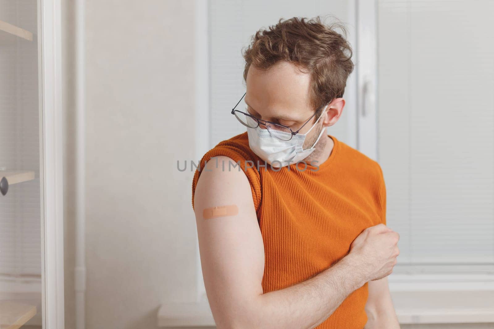 Caucasian young man showing his shoulder with bandage after getting a vaccination during covid-19 immunization program