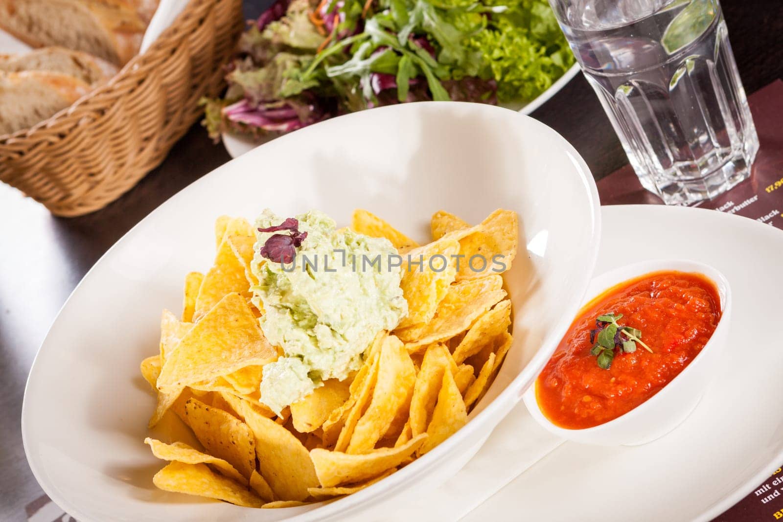 Corn chips nachos with guacamole and salsa dipp in a bowl on a plate