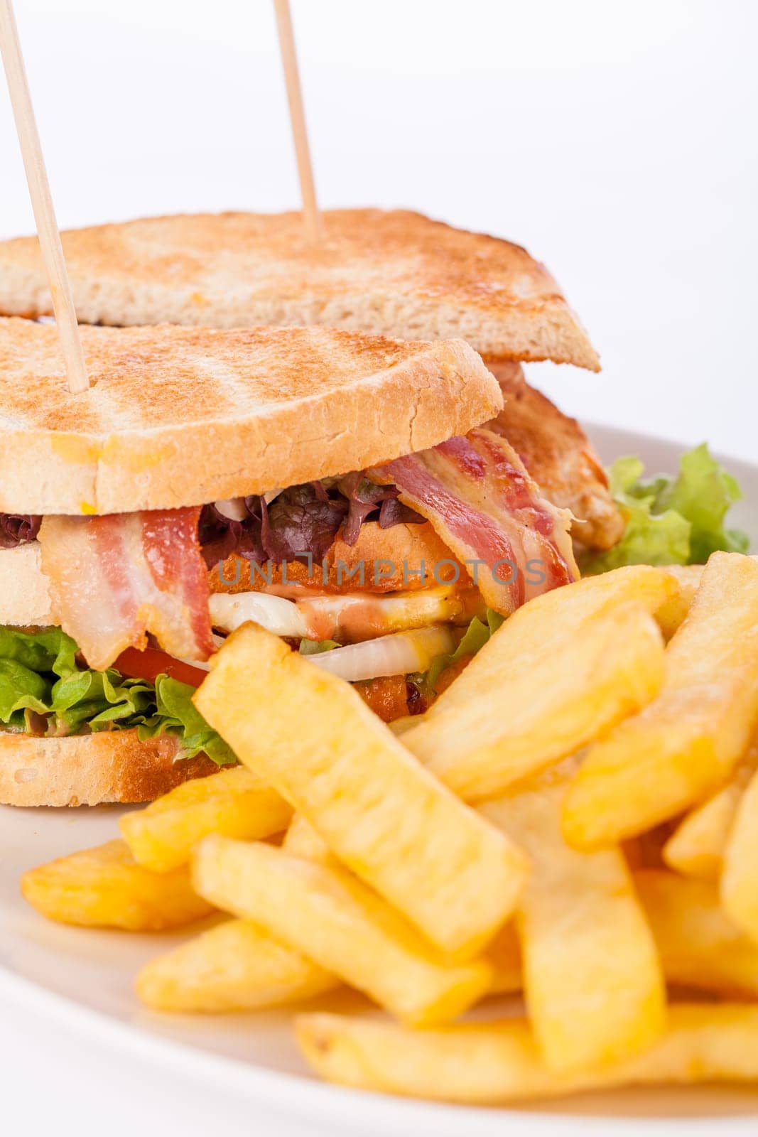 Club sandwich on toasted white bread with bacon and fries fried fries on a plate isolated against a white background